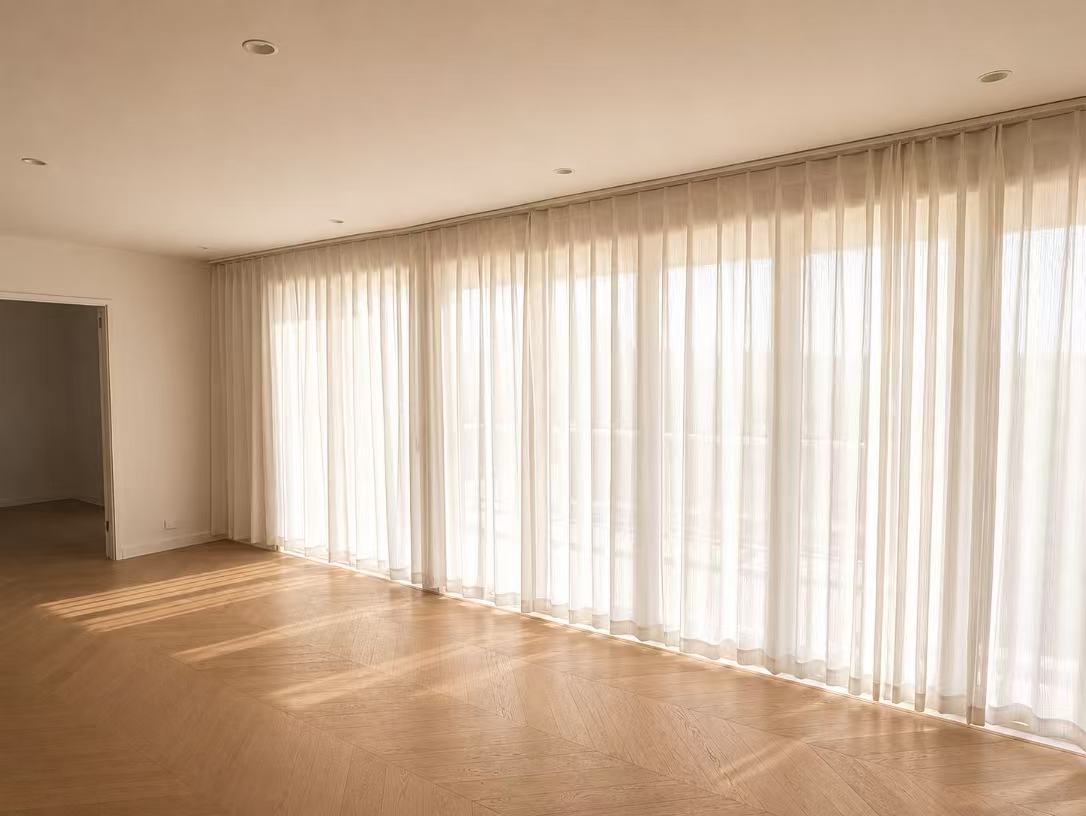 Full wall of cream sheer curtains glowing with backlit afternoon sun over a herringbone floor